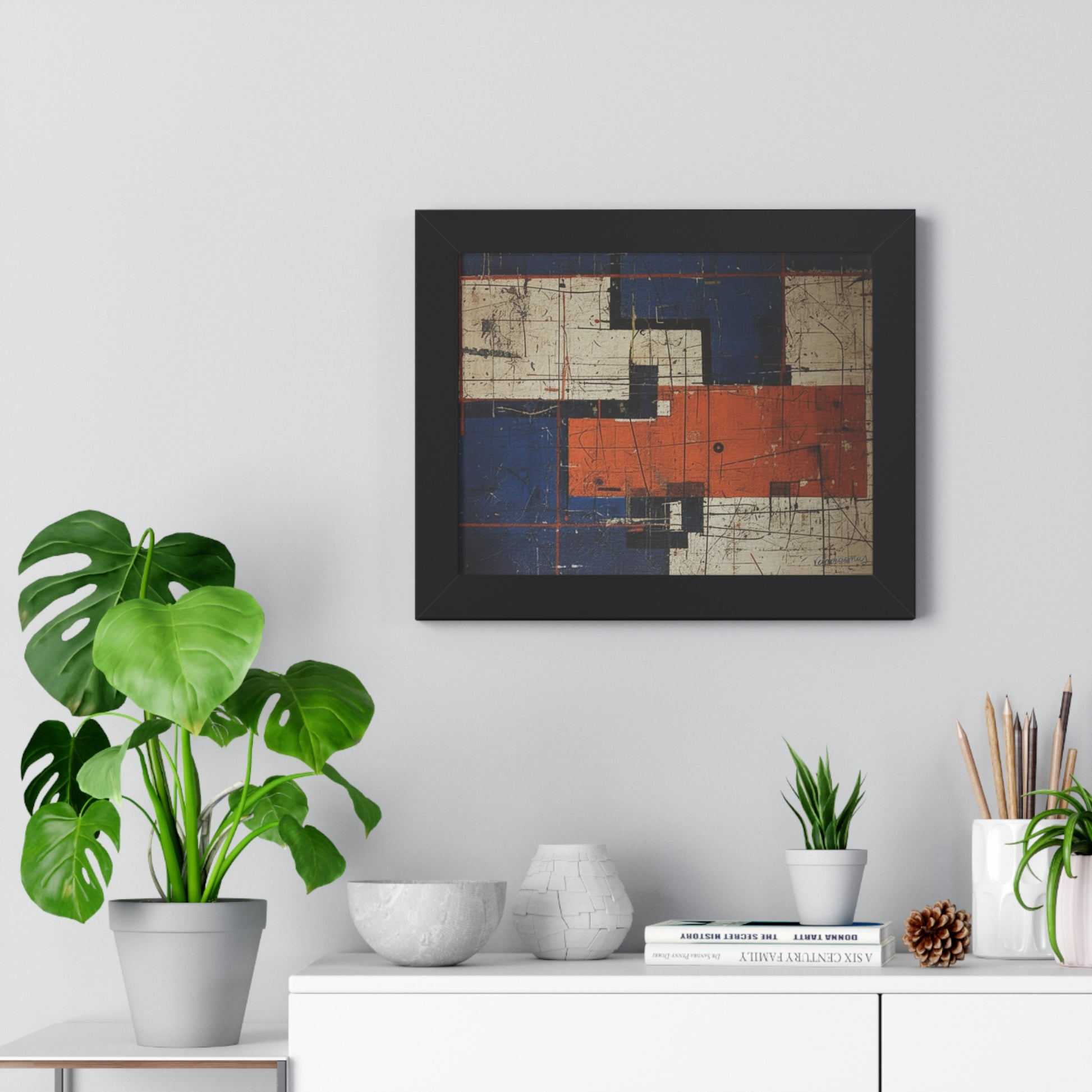 Framed abstract art piece on a wall above a white cabinet with decorative items.